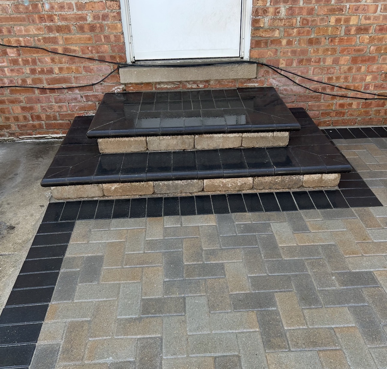 Finished black-capped paver steps with herringbone landing at a brick rear entry